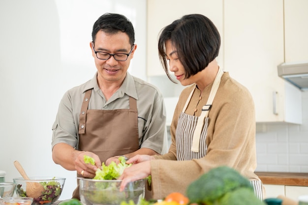 Una coppia asiatica felice, marito e moglie, stanno facendo insieme una ciotola di insalata in cucina.