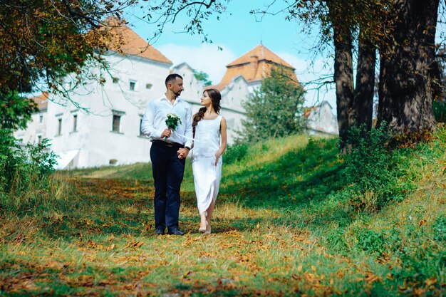 Una coppia cammina in un parco autunnale vicino al castello. Novelli sposi.