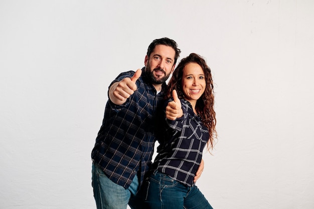 Una coppia caucasica adulta in camicie a quadri in piedi e mostrando i pollici fino alla telecamera e sorridendo su uno sfondo bianco.