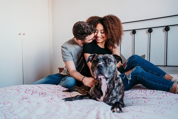Una coppia che ride seduta a letto con un cane a casa