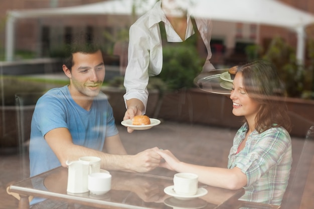 Una coppia che si tiene per mano mentre cameriera che serve cibo