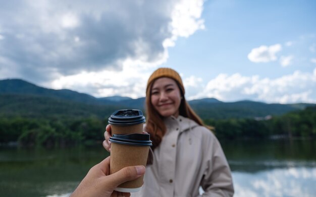 Una coppia che tiene e fa tintinnare la tazza di caffè insieme mentre viaggia sulle montagne e sul lago