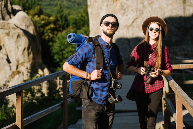 Una coppia che viaggia in montagna con indosso abiti hipster con zaino, macchina fotografica vintage e binocolo