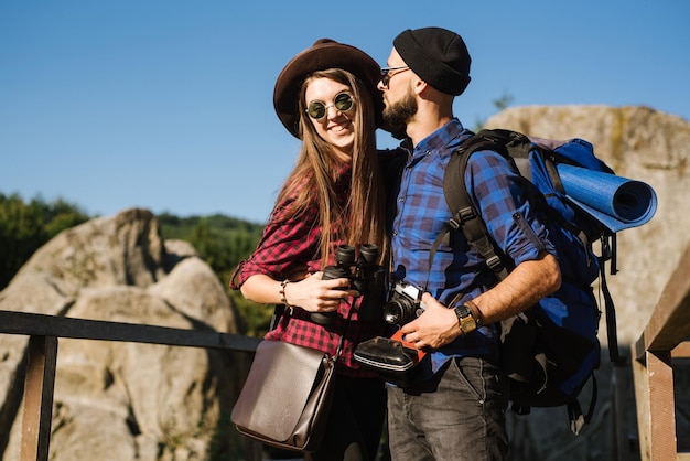 Una coppia che viaggia in montagna con indosso abiti hipster con zaino, macchina fotografica vintage e binocolo