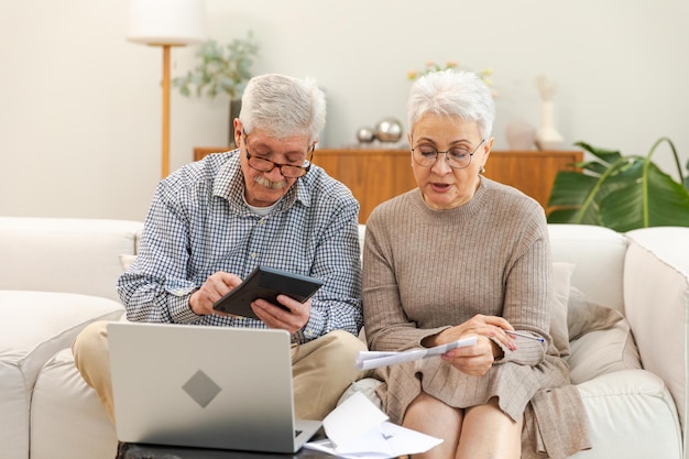 Una coppia di anziani di mezza età si siede con un portatile e un documento cartaceo un uomo maturo più anziano una donna che legge la carta bi