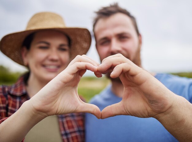 Una coppia di contadini sostiene la sostenibilità facendo un segno del cuore d'amore con le mani all'aperto in una fattoria biologica Attivisti felici e spensierati con la passione per l'agricoltura sostenibile e biologica