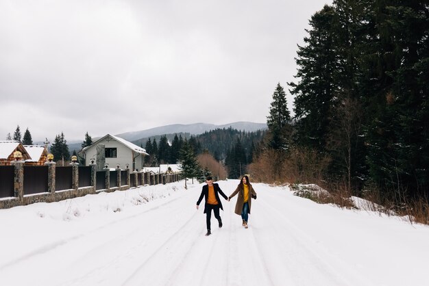 Una coppia di giovani cammina tenendosi per mano lungo una strada innevata