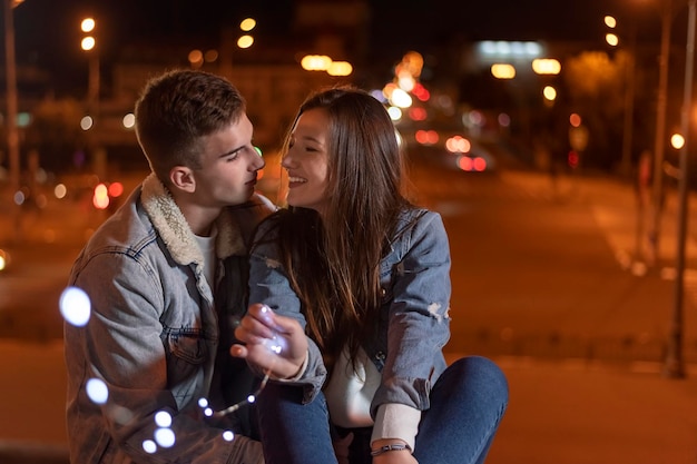 Una coppia di innamorati è seduta sullo sfondo della città di sera con una ghirlanda nelle loro mani