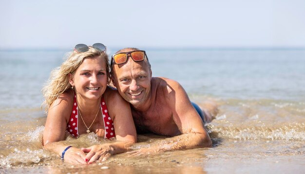 Una coppia di mezza età sdraiata su una spiaggia in riva al mare durante una calda giornata estiva che trascorre una vacanza insieme