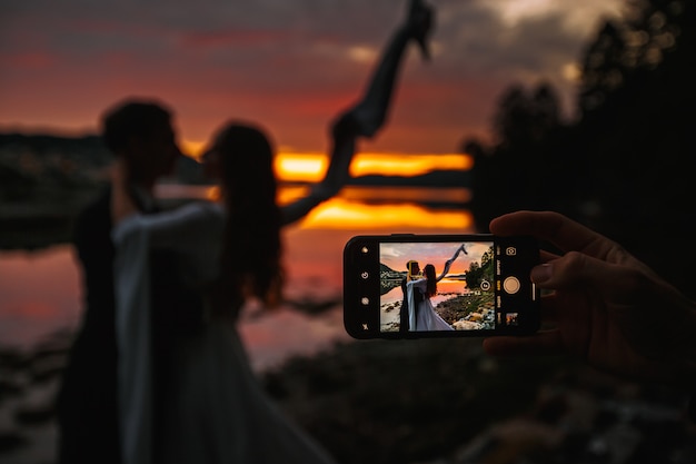 Una coppia di sposi in piedi accanto a un fiume. Sullo sfondo, il villaggio al tramonto, sparando al telefono