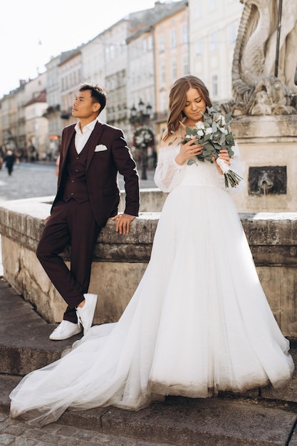 Una coppia di sposi internazionali, una sposa europea e uno sposo asiatico camminano insieme per la città