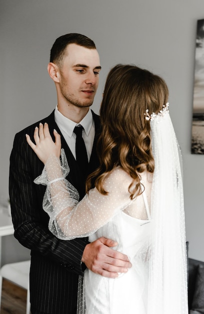 Una coppia di sposi sta vicino a un muro semplice. bellissimi abiti da sposa. sposa con in mano un mazzo di fiori. giovane famiglia. gente felice. momento gioioso.