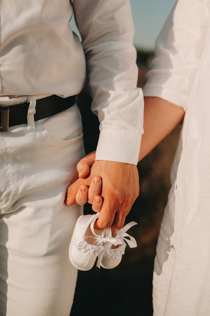 Una coppia di sposi vestita in abiti bianchi cammina mano nella mano mentre tiene un paio di scarpe per bambini