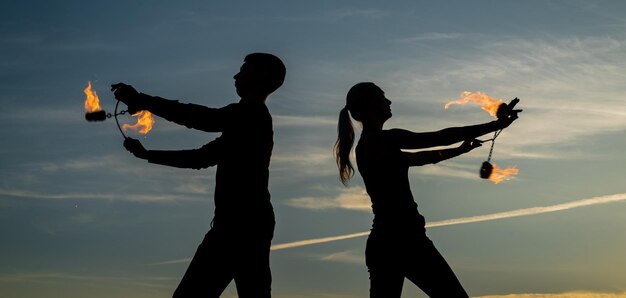 Una coppia di uomini e donne esegue la danza del poi bruciante durante le esibizioni di fuoco in sagome scure sull'idilliaco cielo serale all'aperto infuocato