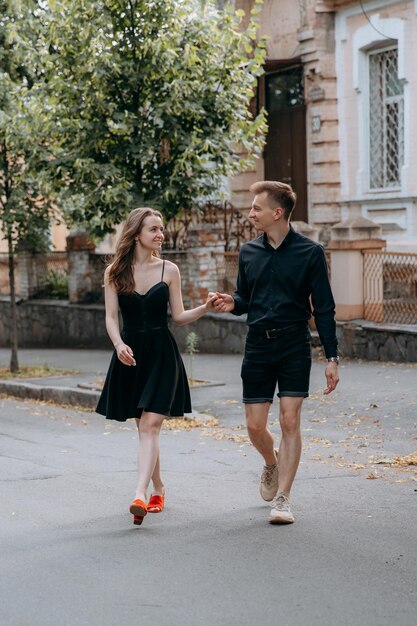 Una coppia elegante e innamorata in abiti neri cammina per le strade e ride.