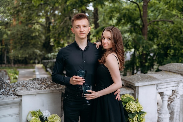 Una coppia elegante in nero è in piedi sul balcone con un bicchiere di vino in mano