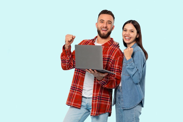 Una coppia felice con un portatile che celebra sullo sfondo blu