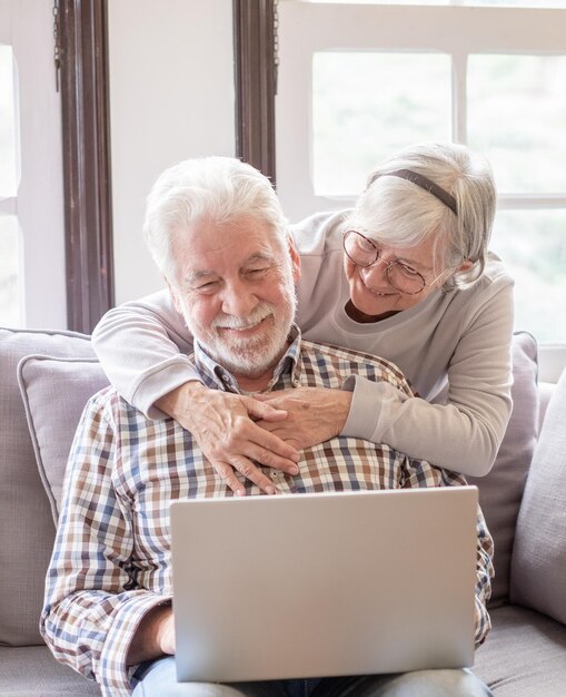 Una coppia felice di 70 anni con i capelli bianchi a casa che usa il portatile insieme per fare acquisti online