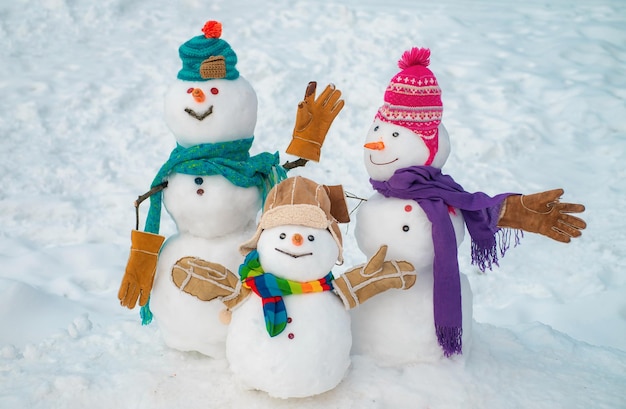 Una coppia felice di pupazzi di neve e un bambino pupazzo di neve con un regalo di Natale in piedi nel paesaggio natalizio invernale