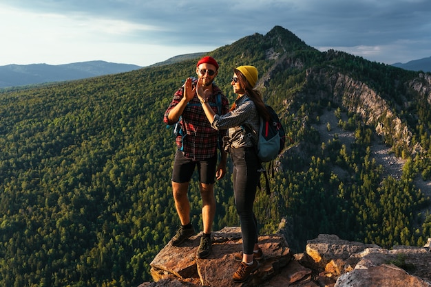 Una coppia felice in montagna ammira gli splendidi panorami. Un uomo e una donna con gli zaini sulla montagna ammirano la vista panoramica. I viaggiatori amano scalare la montagna al tramonto. Copia spazio