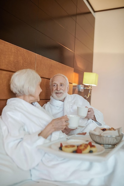 Una coppia felice senior che gode della colazione mentre sta a letto