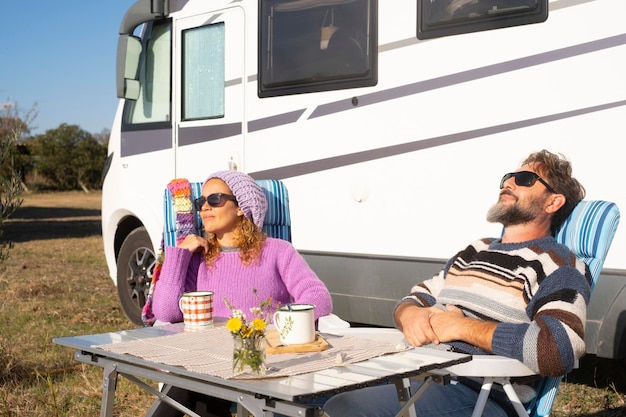 Una coppia felice si gode il turismo nomade di viaggio seduto al tavolo all'aperto fuori da un camper Noleggiare il concetto di veicolo per le vacanze Invecchiare insieme allo stile di vita di un furgone avventuroso Sorriso di uomo e donna