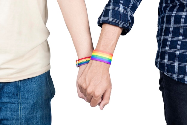 Una coppia gay con un braccialetto con bandiera arcobaleno LGBT che si tiene per mano insieme in piedi