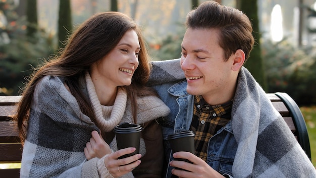 Una coppia gioiosa in un appuntamento romantico nel parco naturale che copre con una coperta tiene una bevanda calda e spensierata