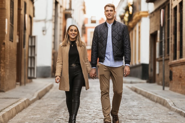 Una coppia in abiti autunnali passeggia sorridendo per strada Persone