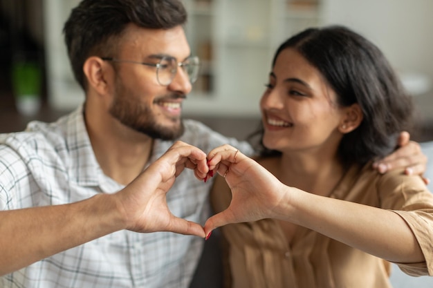 Una coppia indiana felice che fa la forma di un cuore con le dita. Focalizzazione selettiva sulle mani sullo sfondo sfocato.