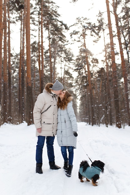 Una coppia innamorata cammina con il cane nella foresta invernale