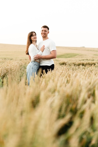 Una coppia innamorata sta in mezzo a un campo di grano e si tiene per mano. un ragazzo e una ragazza stanno camminando nella natura. vacanza fuori città