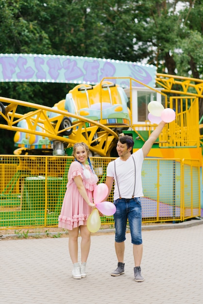 Una coppia romantica che passeggia nel parco divertimenti. La ragazza sorride, accettando un regalo di palloncini