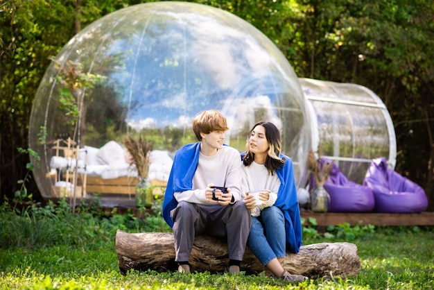 Una coppia seduta vicino a una tenda a bolle trasparente al glamping