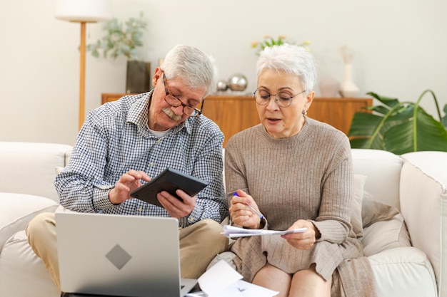 Una coppia senior di mezza età si siede con un computer portatile e un documento cartaceo, un uomo maturo e una donna che leggono la carta