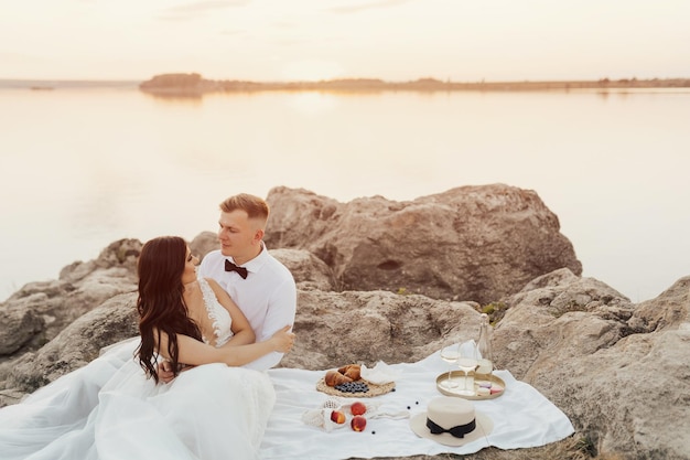 Una coppia si siede su una coperta di fronte a un lago e il tramonto è visibile.