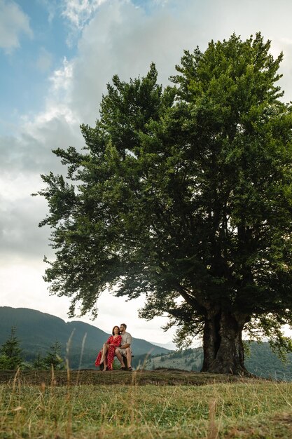 Una coppia si siede su una panchina vicino a un grande vecchio faggio con vista sulle montagne