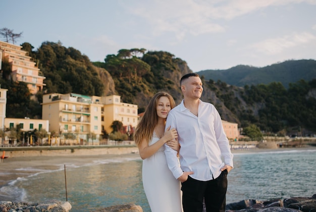 Una coppia si trova su una roccia di fronte a una montagna e al mare.