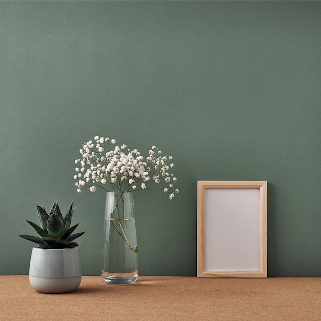 Una cornice, un vaso di fiori bianchi e una pianta in vaso stanno su un pavimento di sughero