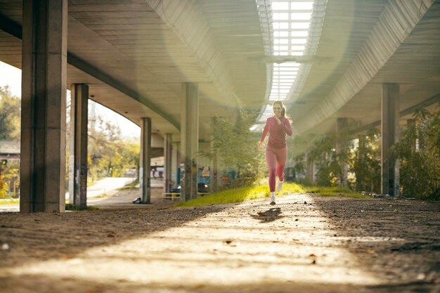 Una corridore donna veloce corre in esterno urbano verso la telecamera.