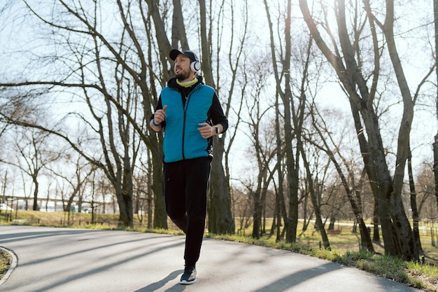 Una corsa mattutina nello scenario del parco cittadino di alberi all'inizio della primavera l'uomo vestito calorosamente trascorre del tempo attivo