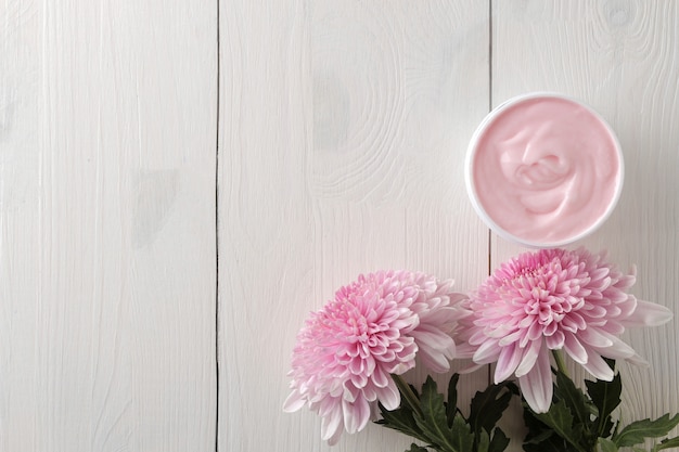 Una crema in un barattolo e fiori di crisantemo su un tavolo di legno bianco con un posto per un'iscrizione.