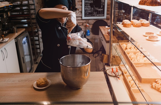 Una cuoca in abito nero mette la crema in una sacca da pasticcere il pasticcere mette la crema in una sacca da cucina