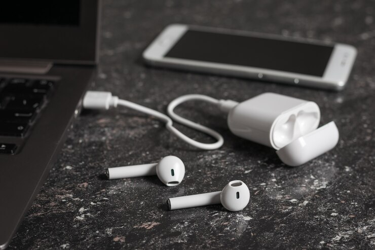Una custodia di cuffie wireless collegate a un laptop e uno smartphone su uno sfondo di pietra. Accessori senza fili moderni.