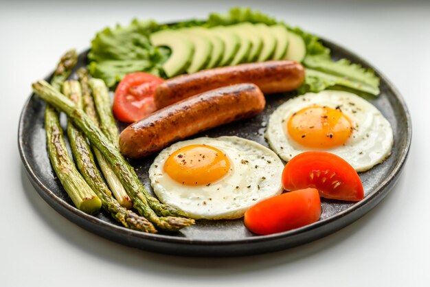 Una deliziosa colazione nutriente con uova fritte salsicce asparagi pomodori avocado spezie ed erbe aromatiche