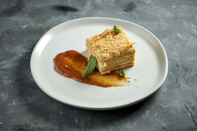 Una deliziosa fetta di millefoglie di dessert francese con strati di pasta sfoglia e fetta di vaniglia o fetta di crema pasticcera, servita in un piatto su una superficie di legno