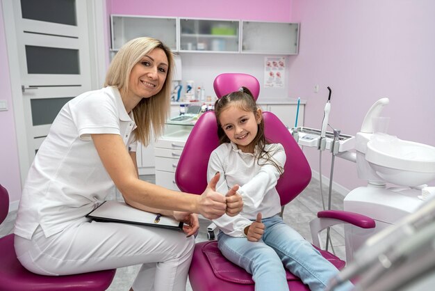 una dentista donna felice sta intervistando una piccola paziente nella clinica dentale per bambini