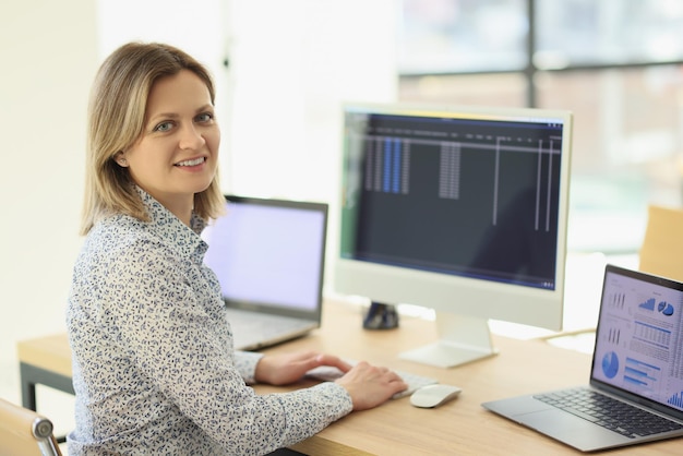 Una dipendente femminile positiva confronta le statistiche sugli schermi dei dispositivi elettronici seduti al tavolo