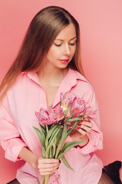 Una dolce donna affascinante con fiori in un vestito rosa su sfondo rosa sorride felicità e fortuna