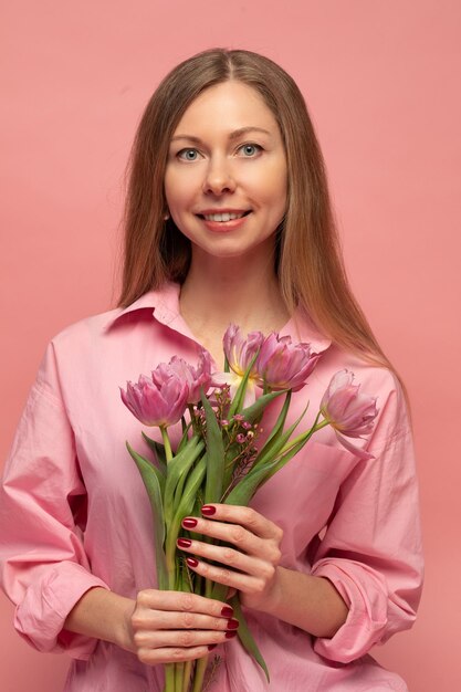 Una dolce donna affascinante con fiori in un vestito rosa su sfondo rosa sorride felicità e fortuna